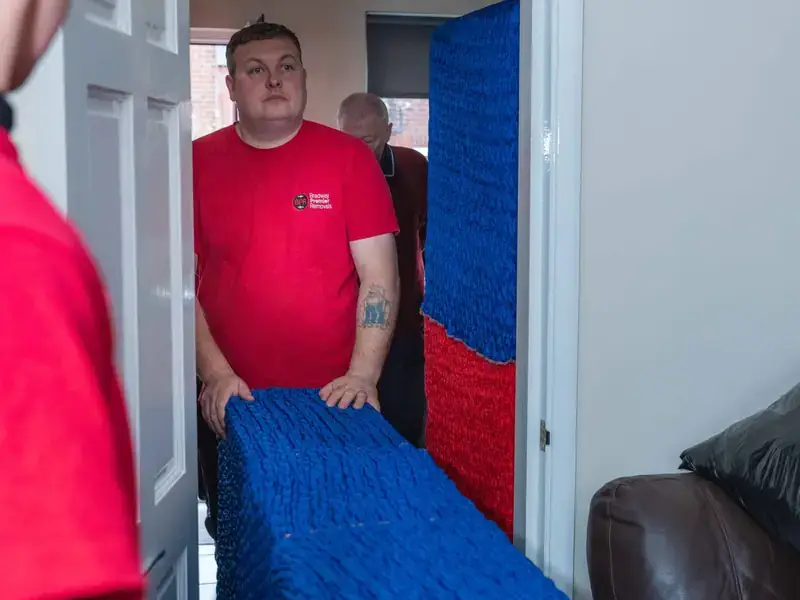 Bradway Premier Removals crew carrying blue wrapped furniture through a hallway during a house removal