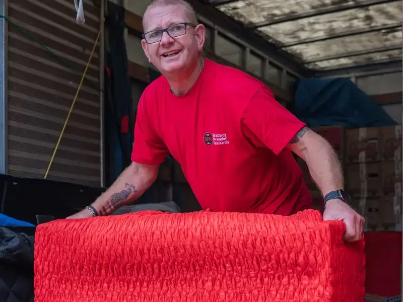 Smiling Bradway Premier Removals crew member loading red wrapped furniture in the van