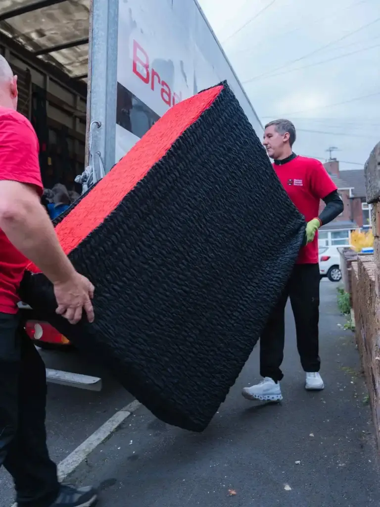 Two Bradway Premier Removals crew members carrying wrapped furniture along the pavement to the van
