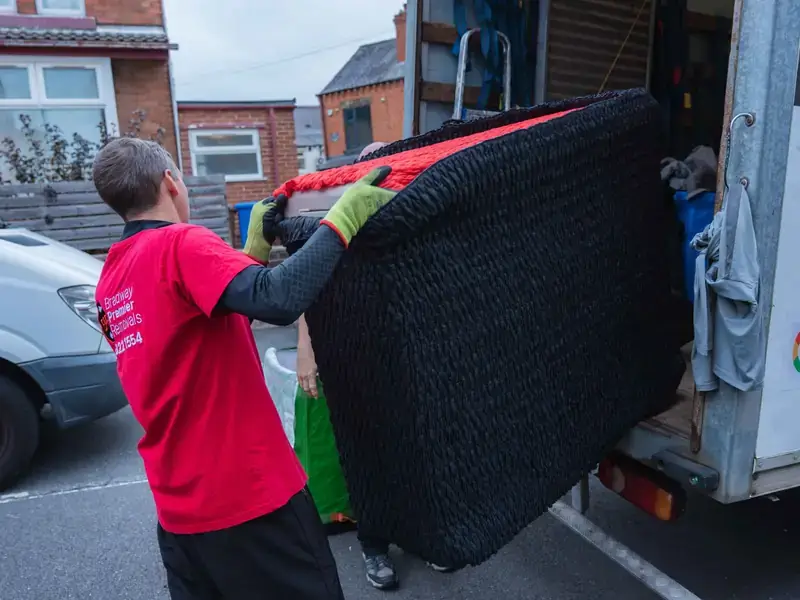 Bradway Premier Removals crew member lifting black wrapped furniture into the removals van on a terraced street