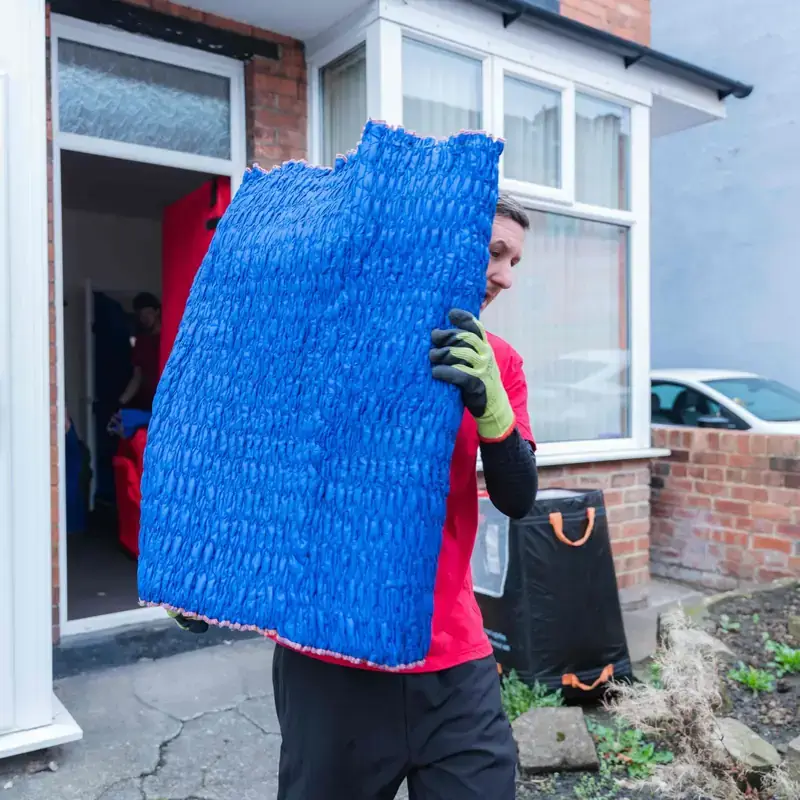 Bradway Premier Removals man and van crew member carrying blue wrapped furniture out of a terraced house