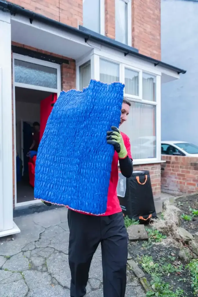 Bradway Premier Removals crew member carrying blue wrapped furniture out of a terraced house