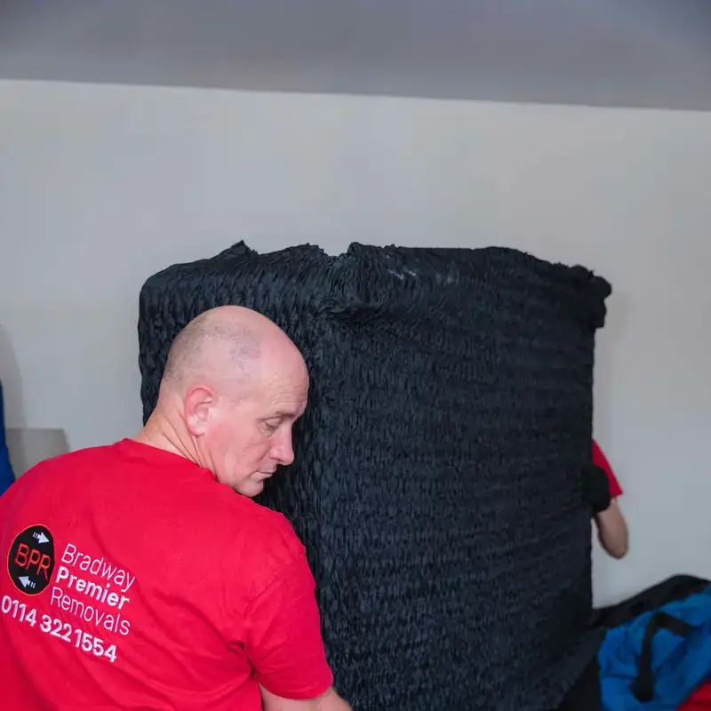 Bradway Premier Removals crew member carrying black wrapped furniture through a room during a house removal