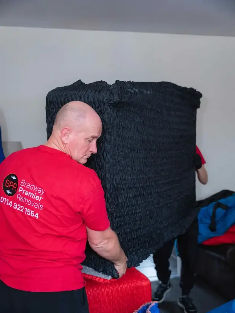 Bradway Premier Removals crew member carrying black wrapped furniture through a room during a house removal