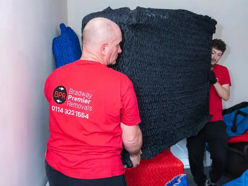 Bradway Premier Removals crew member manoeuvring black wrapped furniture inside a house