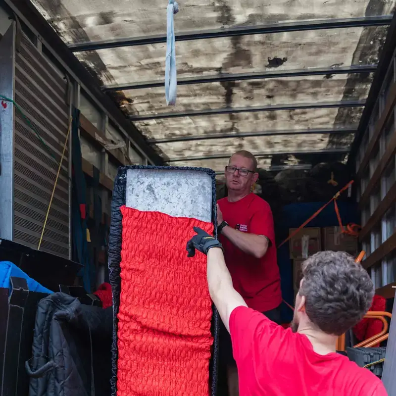 Two Bradway Premier Removals crew members loading red wrapped furniture into the removals van